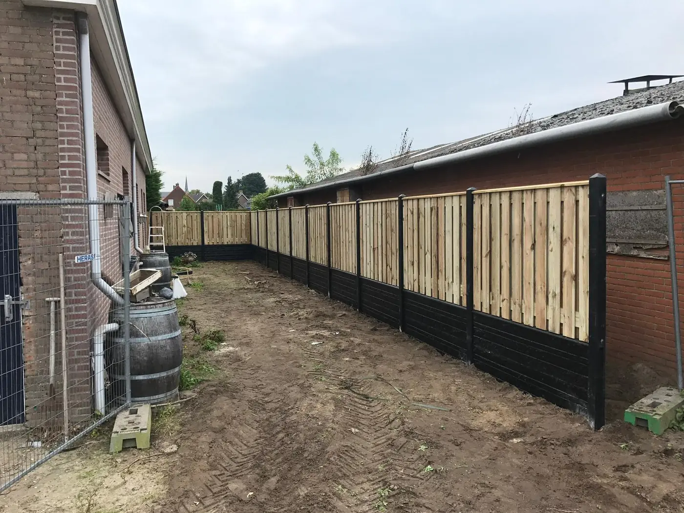 Lange schutting met houten panelen en zwarte palen