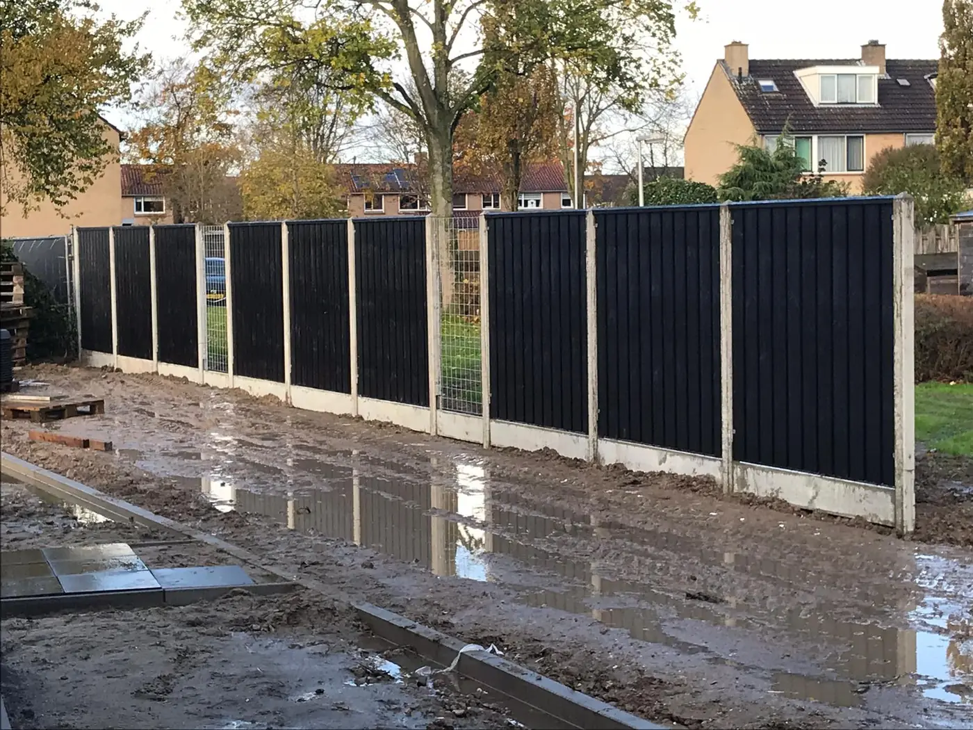 Zwarte houten schutting met betonnen palen langs nieuwe straat