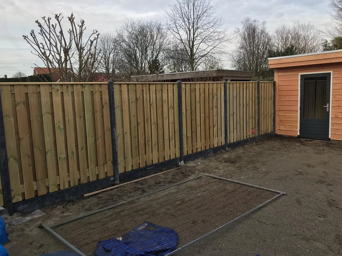 Houten schutting met antracieten betonpalen naast tuinhuis