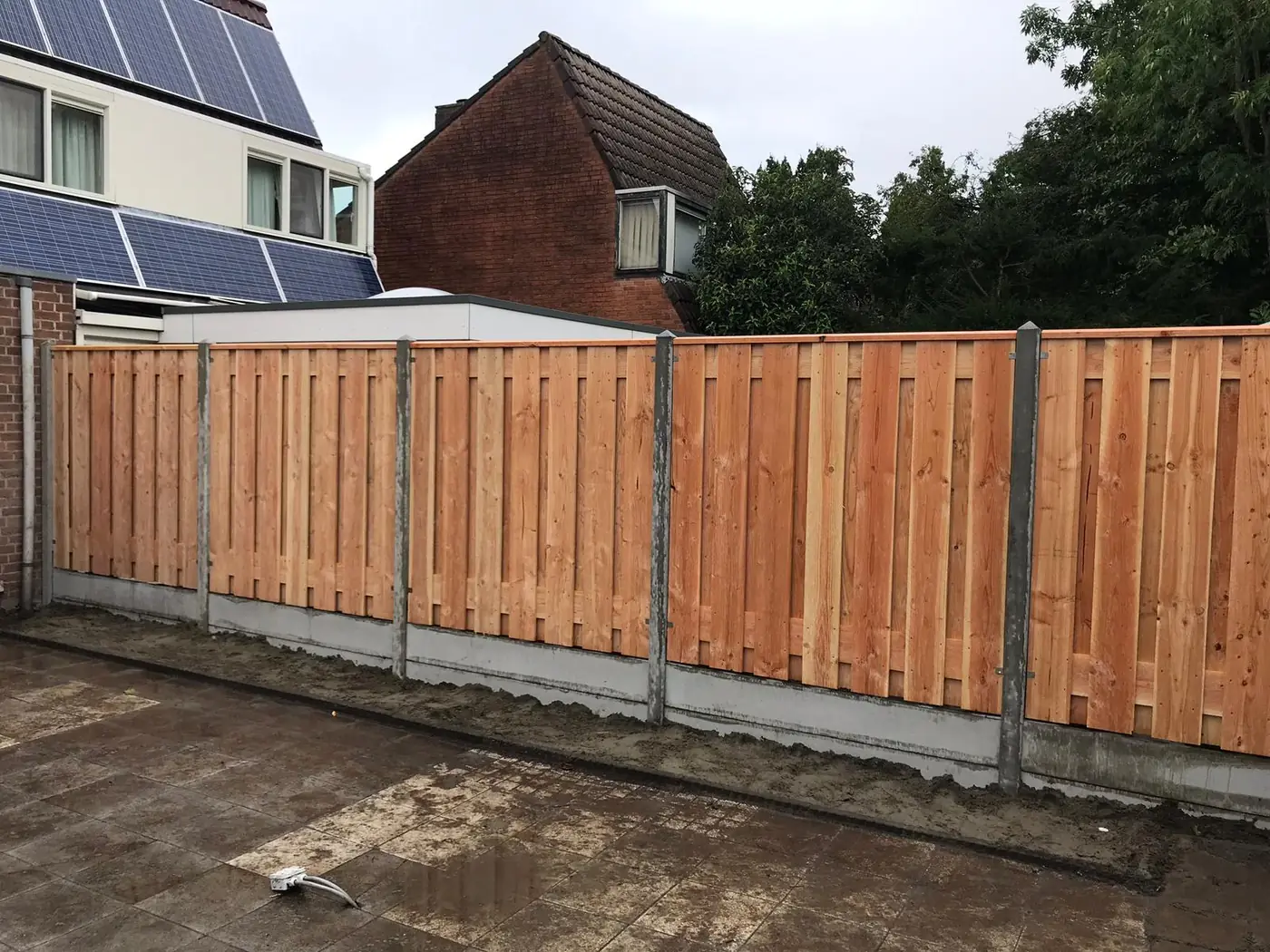 Hardhouten schutting met betonnen palen op bestrating