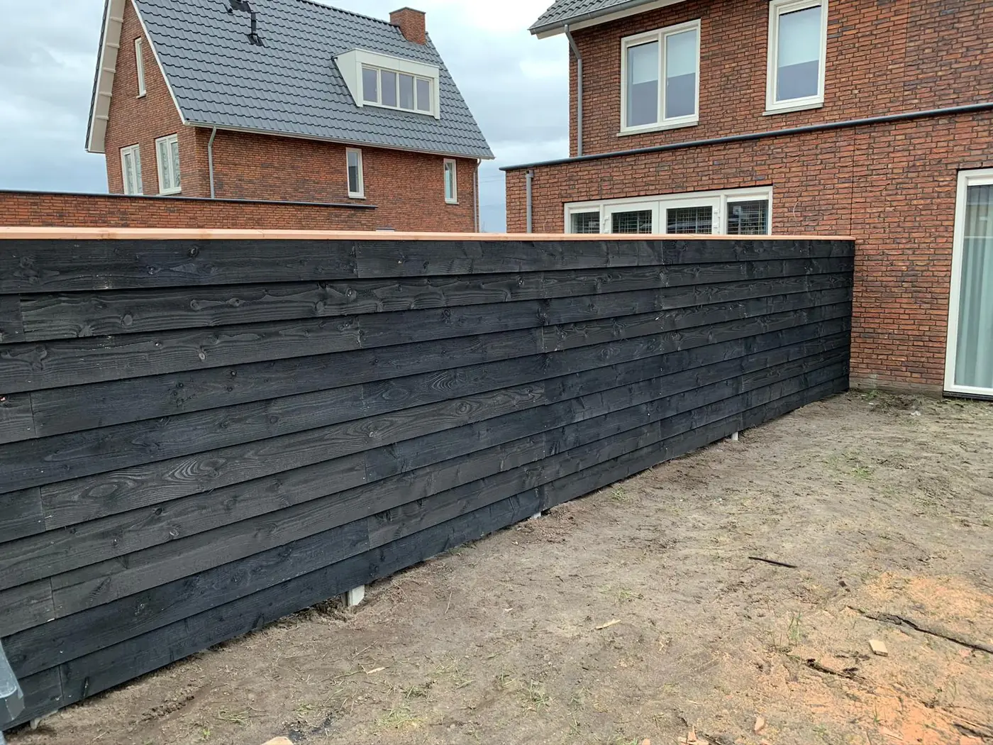 Zwarte horizontale houten schutting met afdekplank