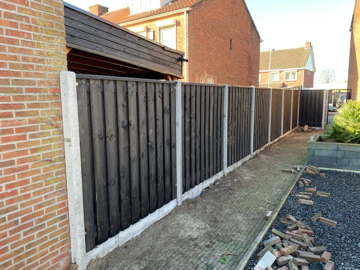 Donkere houten schutting langs zijpad met carport